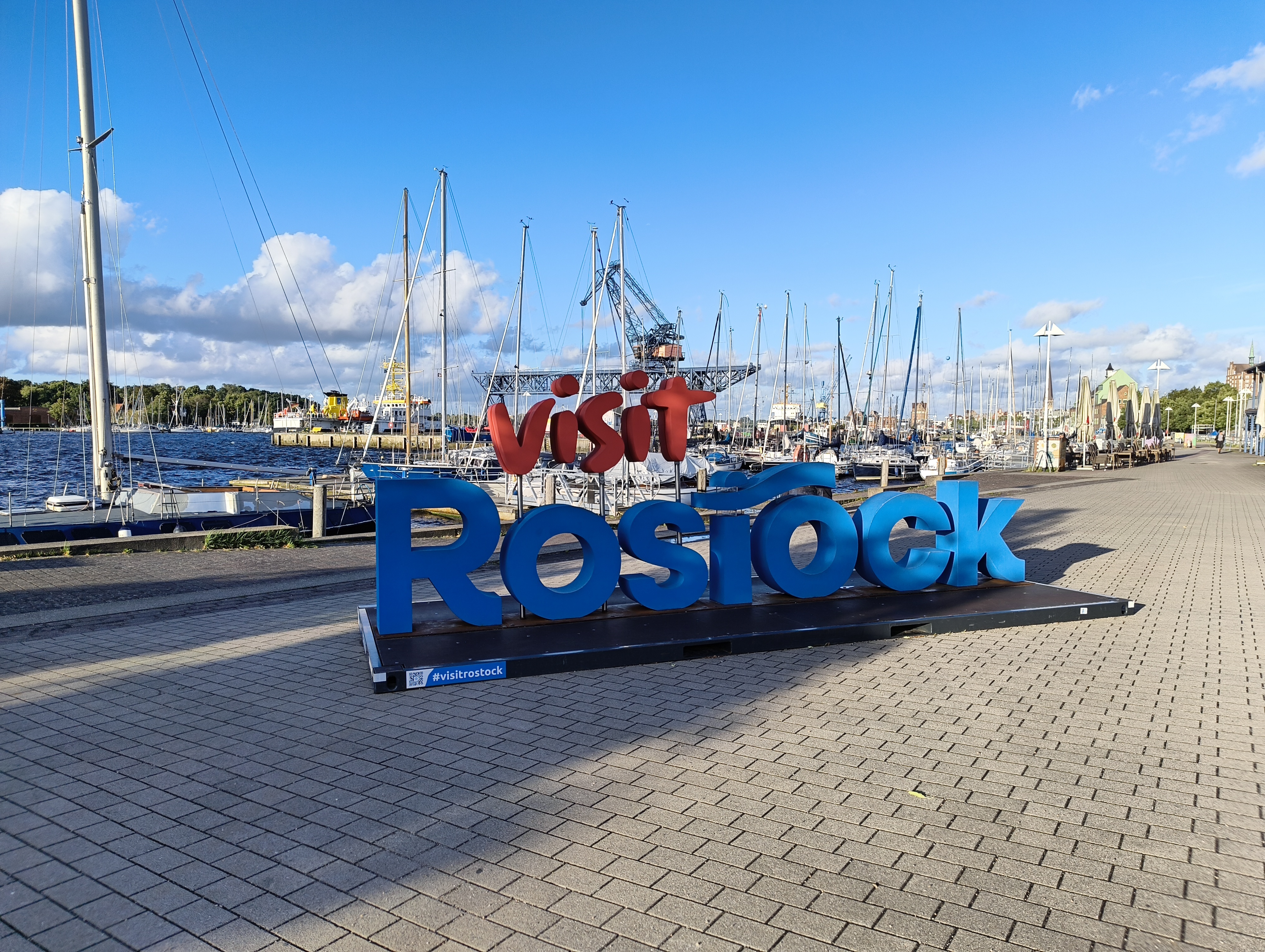 Im Stadthafen die Worte „Visit Rostock“ auf einem kleinen Podest stehend.