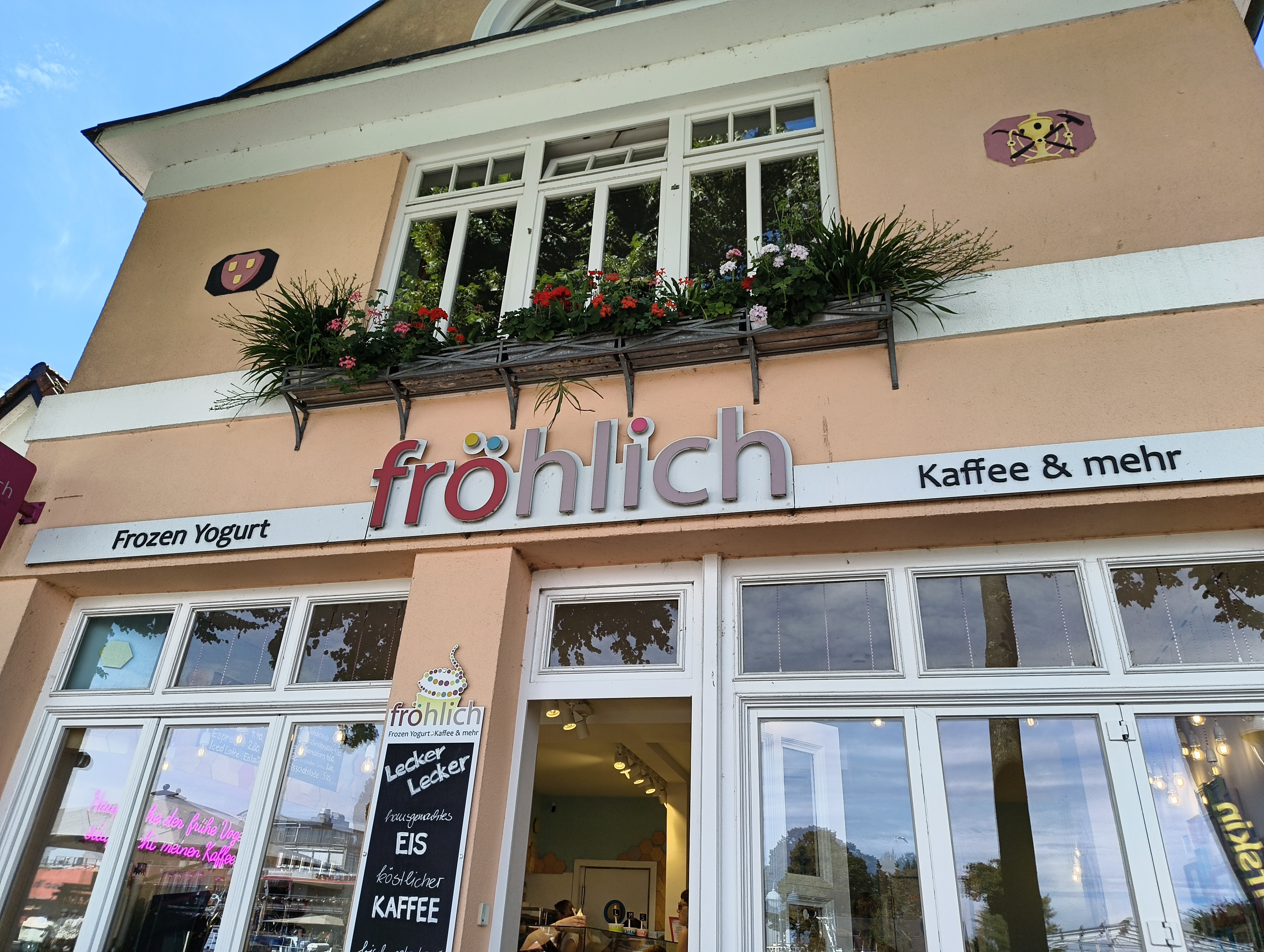 Ein Gebäude von unten nach oben fotografiert. In der Mitte der Schriftzug »fröhlich«. Links der Hinweis auf „Frozen Joghurt“, rechts der Hinweis auf „Kaffee & mehr“.