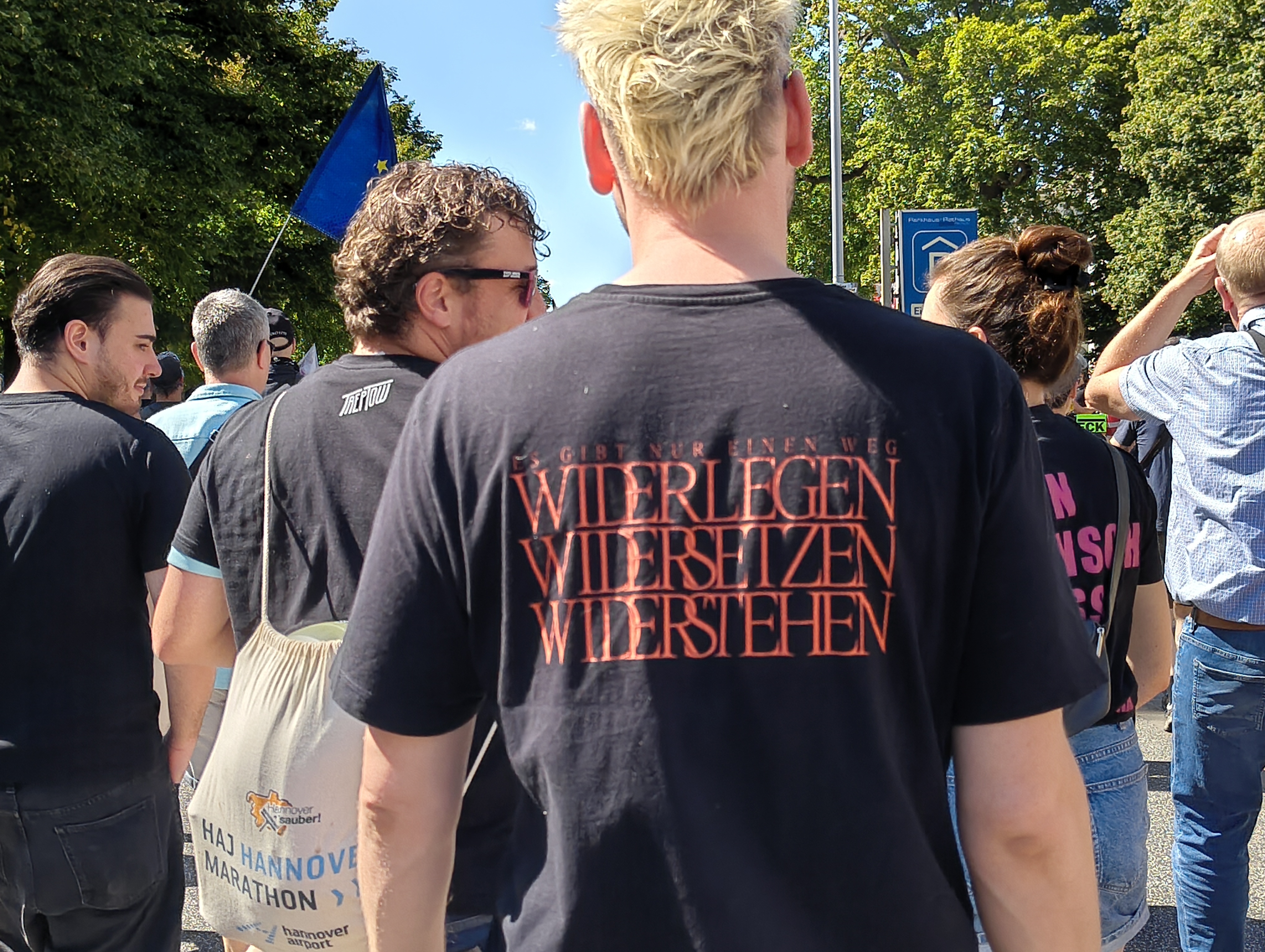 Eine Person mit einem dunklen T-Shirt von hinten aufgenommen. Auf dem T-Shirt der Text: „Es gibt nur einen Weg · Widerlegen · Widersetzen · Widerstehen“.