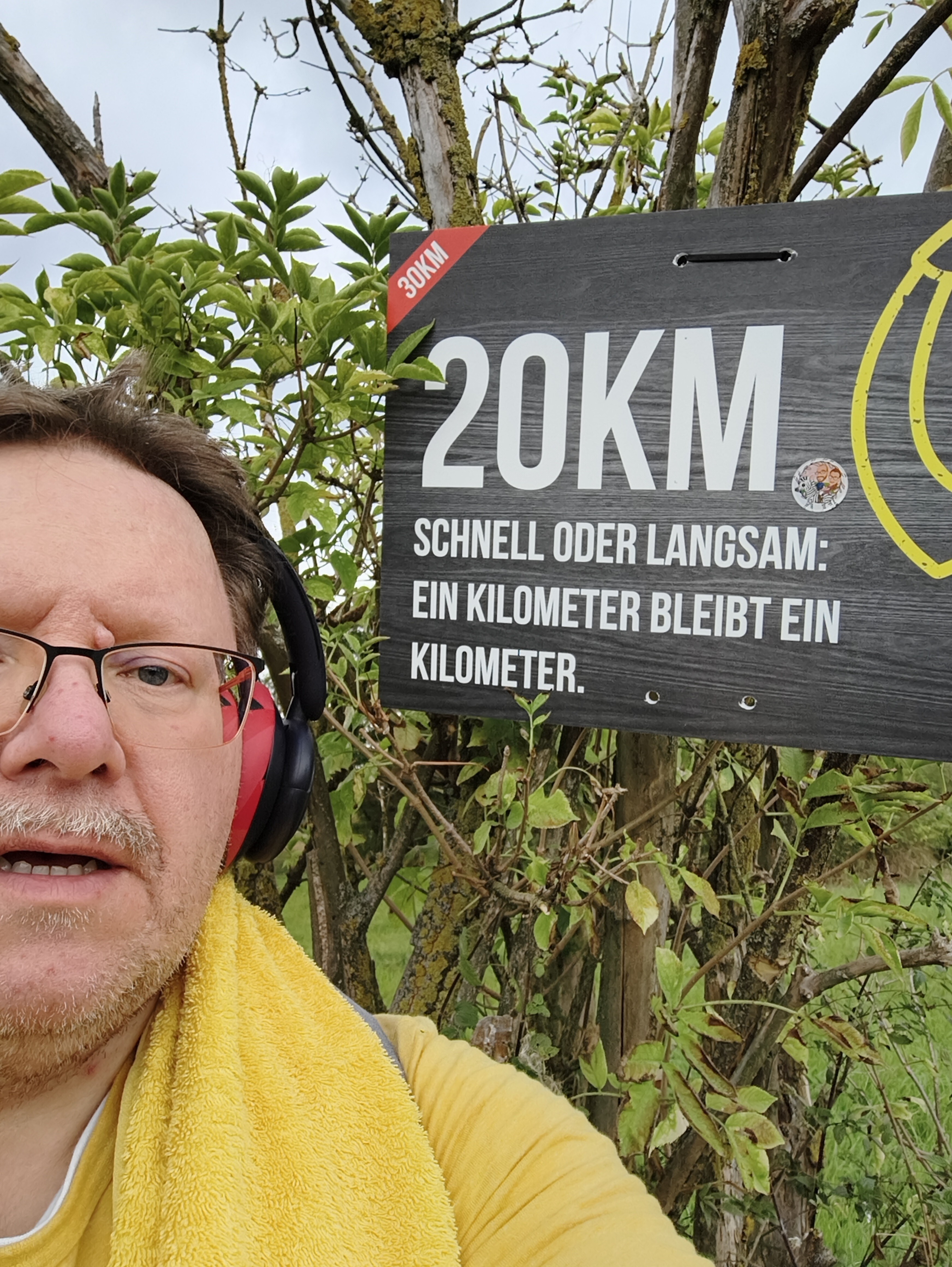 Selfie von mir auf der einen Seite und dem Schild mit der Aufschrift '20 km · Schnell oder langsam: ein Kilometer bleibt ein Kilometer' auf der anderen Seite.