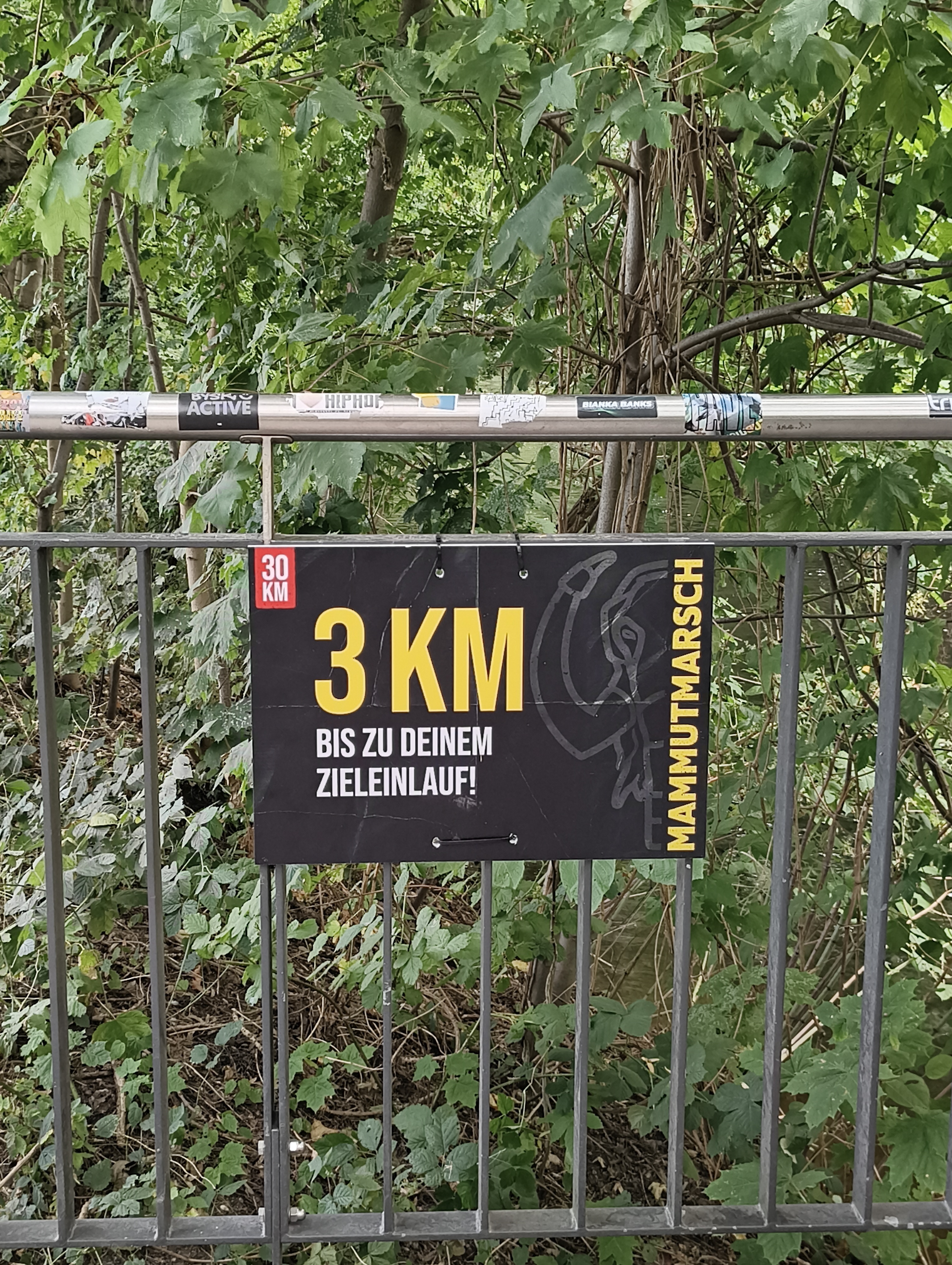 Schild hängt an einem Gitter: '3 km bis zu deinem Zieleinlauf'.