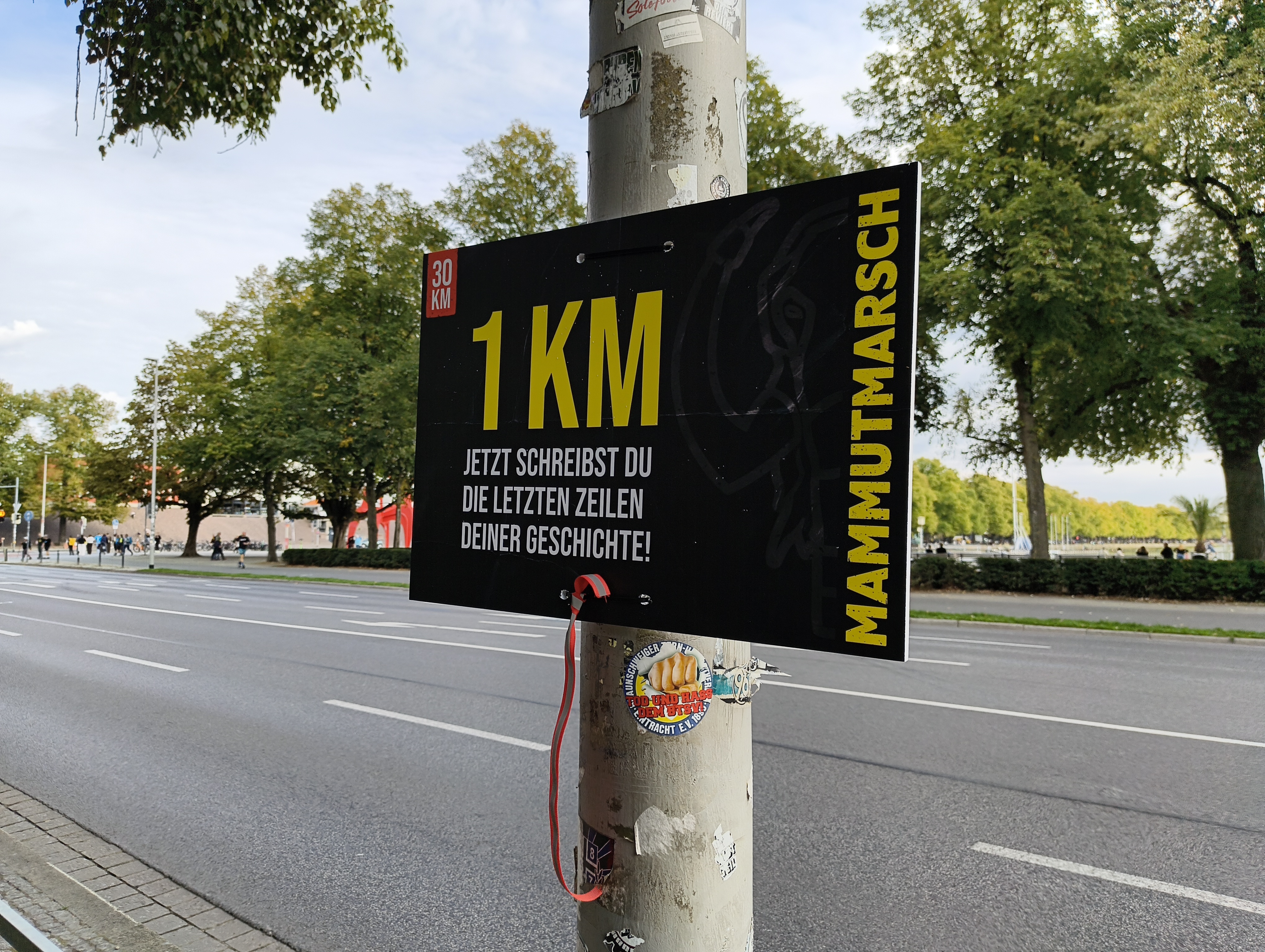 Schild an einem Laternenpfahl: '1 km · Jetzt schreibst du die letzten Zeilen deiner Geschichte'