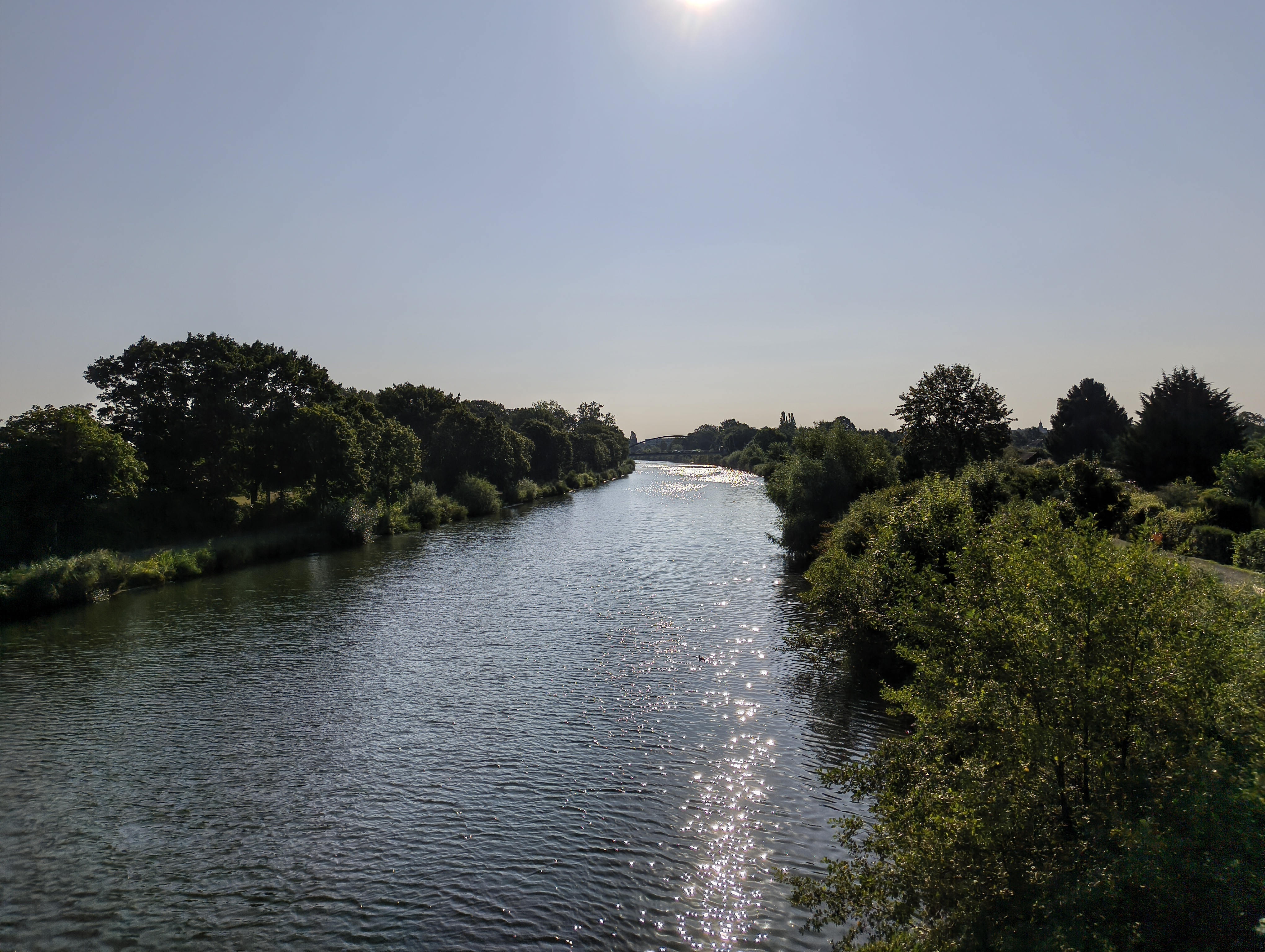 Seitlicher Blick von der Tannebergallee-Brücke auf den Mittellandkanal. Die Sonne spiegelt sich auf den Wogen des Wassers. Links und rechts des Kanals sattes Grün von Grünflächen, Büschen und Bäumen.