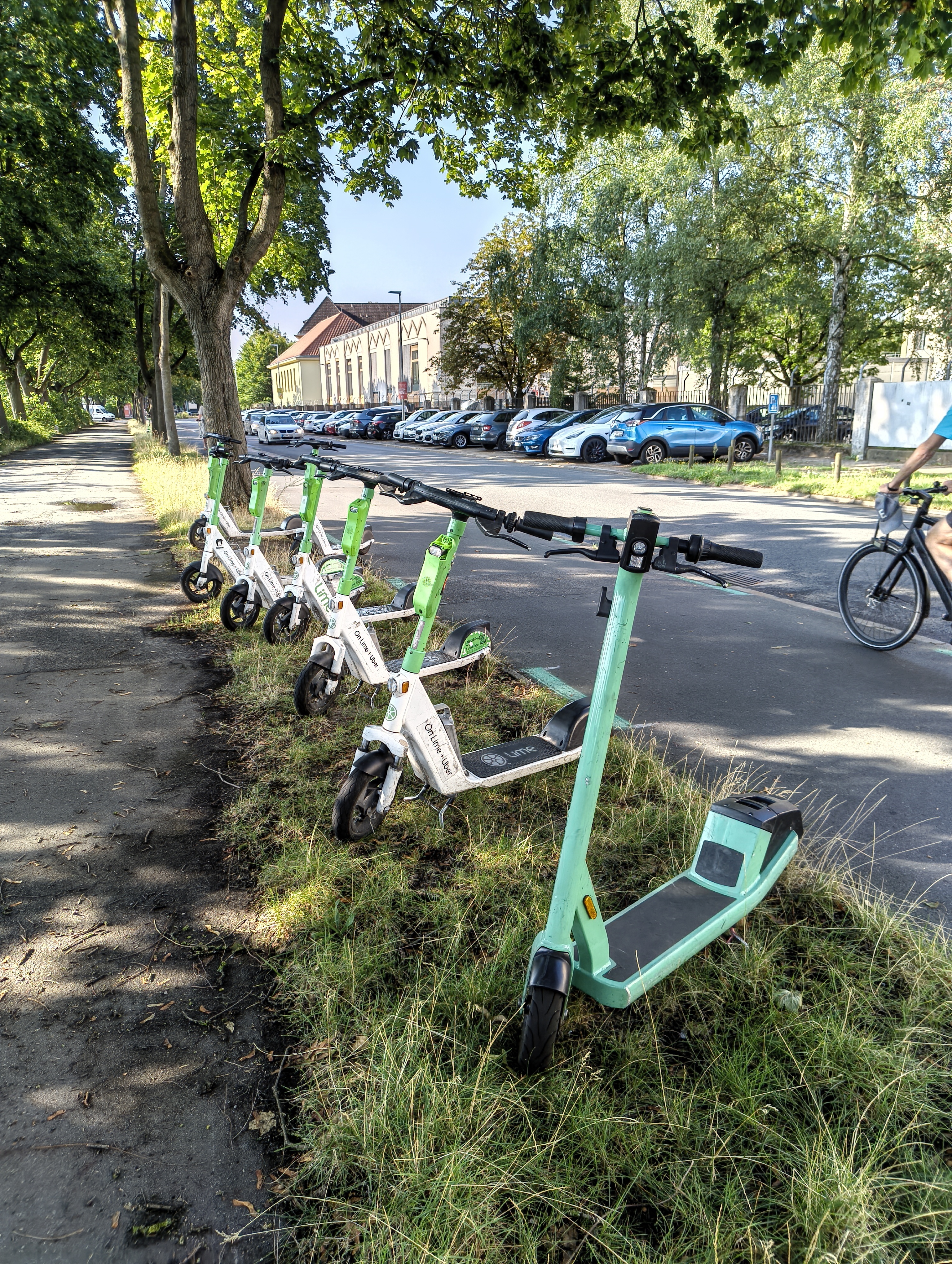 Sieben eScooter, vorwiegend vom Anbieter 'OnLime + Uber' stehen in Reihe auf einer Grasfläche.
